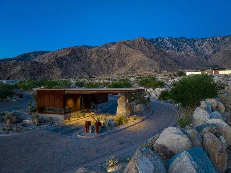 The lit gatehouse at dusk, where the entry drive curves between boulders.